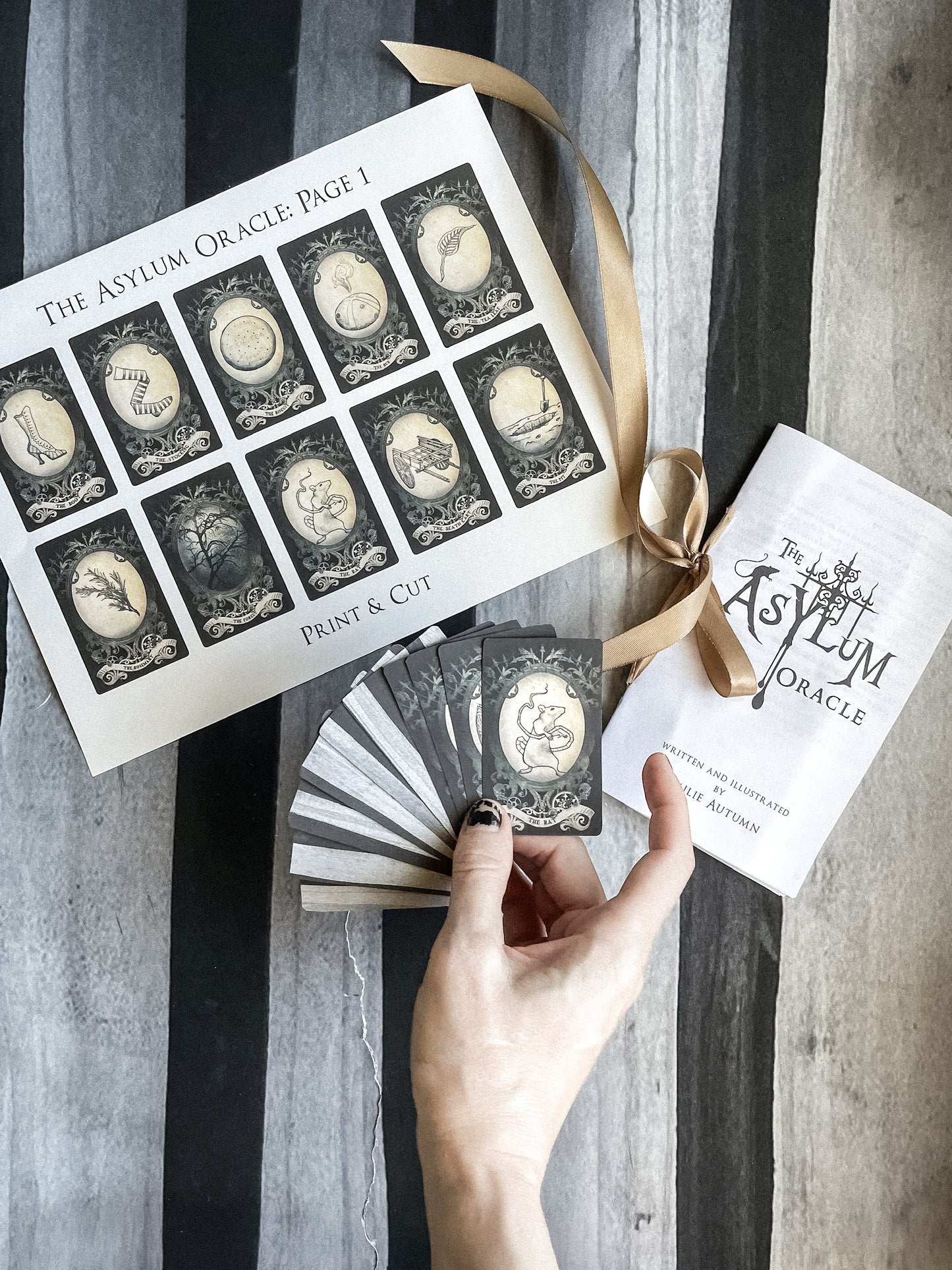The Asylum Oracle cards with packaging and a hand holding some cards on a striped background