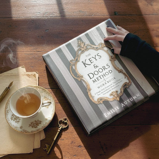 Book titled 'The Keys & Doors Method Workbook' on a wooden surface with a cup of tea and key.