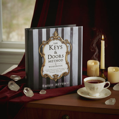 Book titled 'The Keys & Doors Method Workbook' by Emilie Autumn on a table with candles and tea.